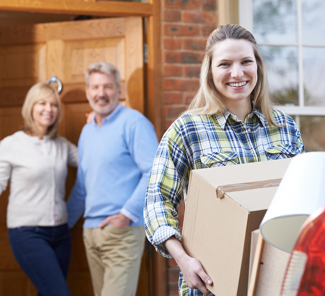 College-aged woman packing car with box as mom and dad look on smiling.